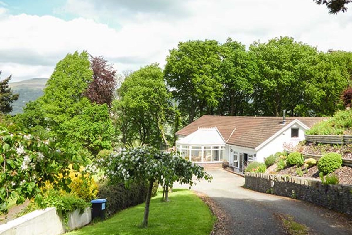 House approached through mature trees with conservatory and Brecon hills beyond at Treetops