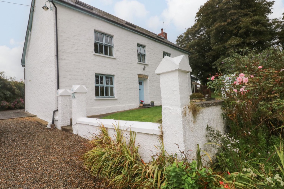 White two-storey farmhouse with blue windows and a walled front garden at Ty Llwyd, Nevern