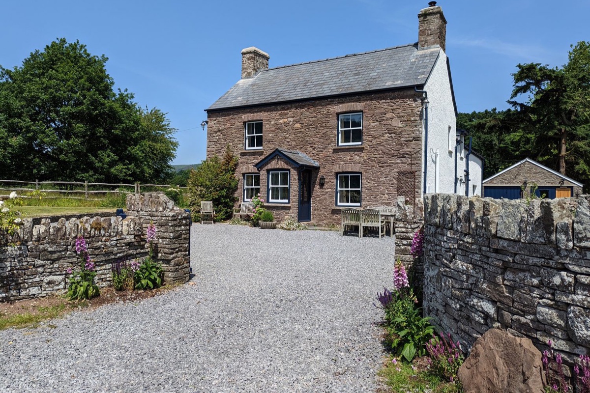 Stone farmhouse front with gravel drive and flower borders at Ty Sinsir