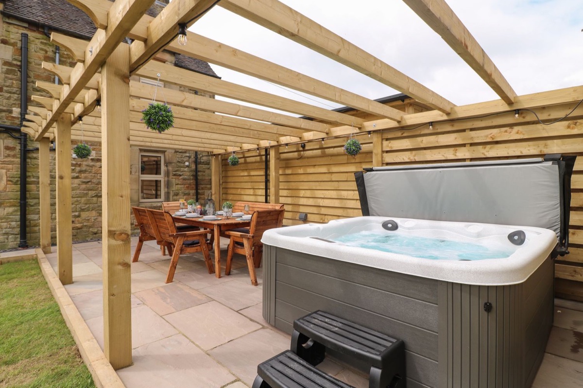Hot tub under a pergola with patio dining by a stone farmhouse at Upper Hurst Farmhouse