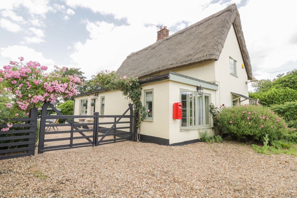 Thatched Waveney Cottage with climbing roses and a gated drive
