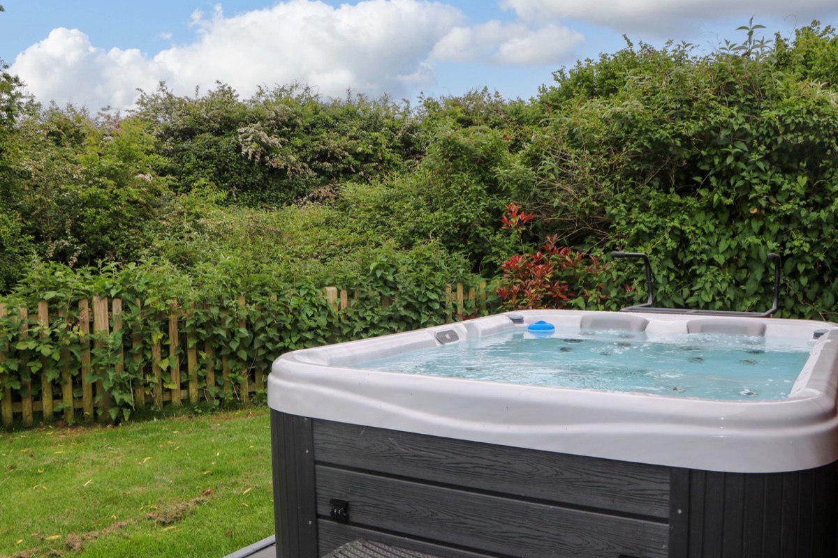 Hot tub on the deck at Willow Pod with a garden and hedge backdrop