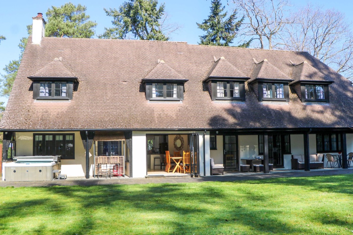 Woodlands House rear exterior with lawn, patio seating and hot tub