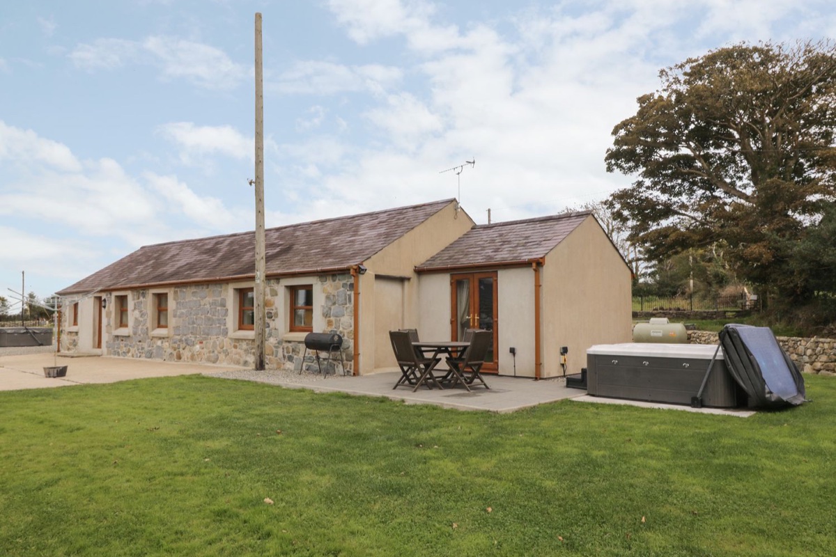 Y Beudy Cottage exterior with lawn, patio seating and hot tub