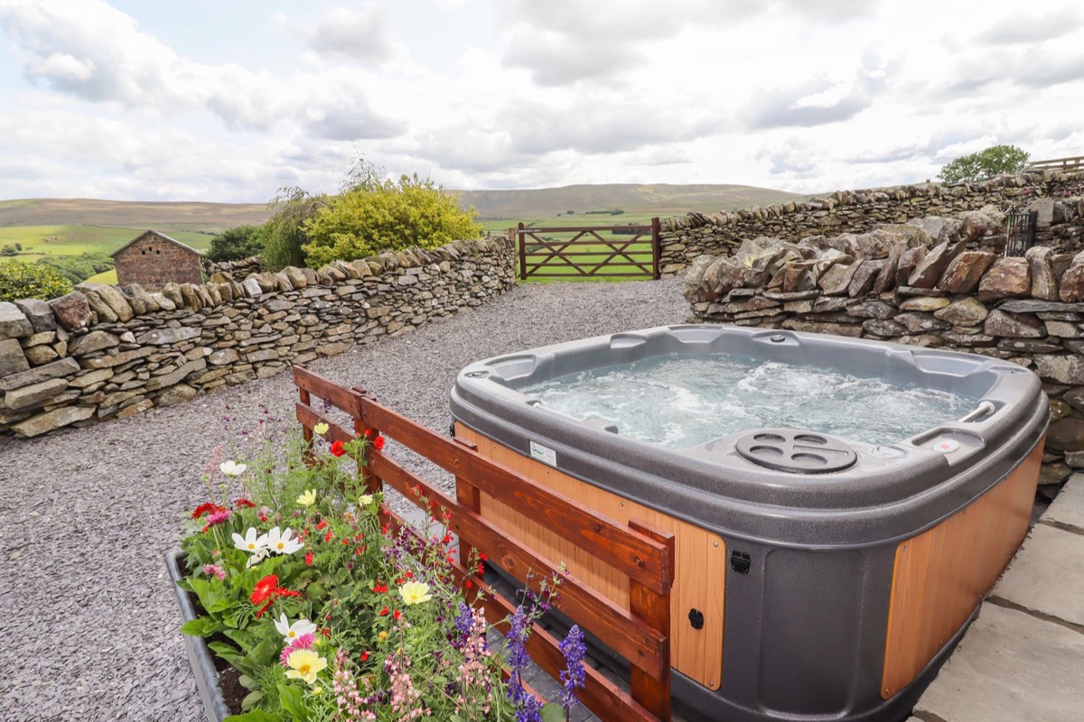 Hot tub outside Y Bwthyn with stone walls and hillside beyond