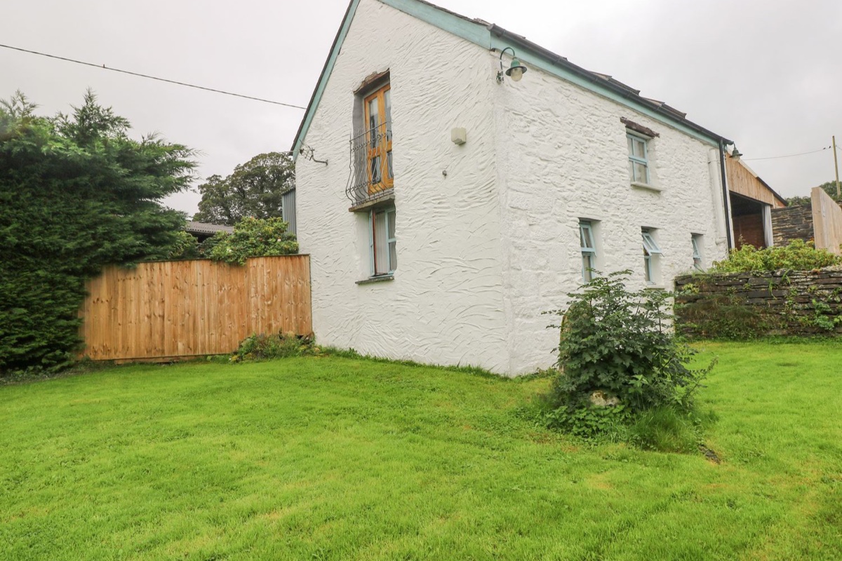 White stone cottage with blue trim and a lawn at Y Cartws
