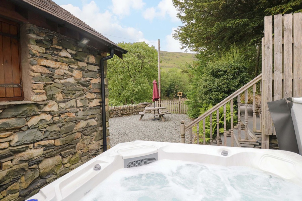 Hot tub on a raised timber deck with the stone cottage and Cumbrian fell hills behind