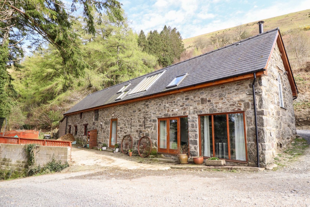 Ysgubor Craig Y Gronfa stone barn exterior below a wooded hillside